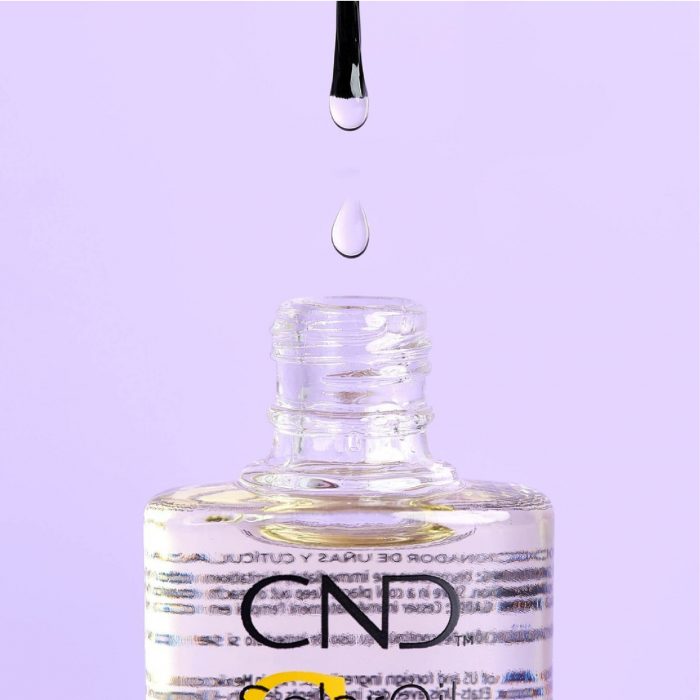 A bottle of cuticle oil with a drop falling from the brush